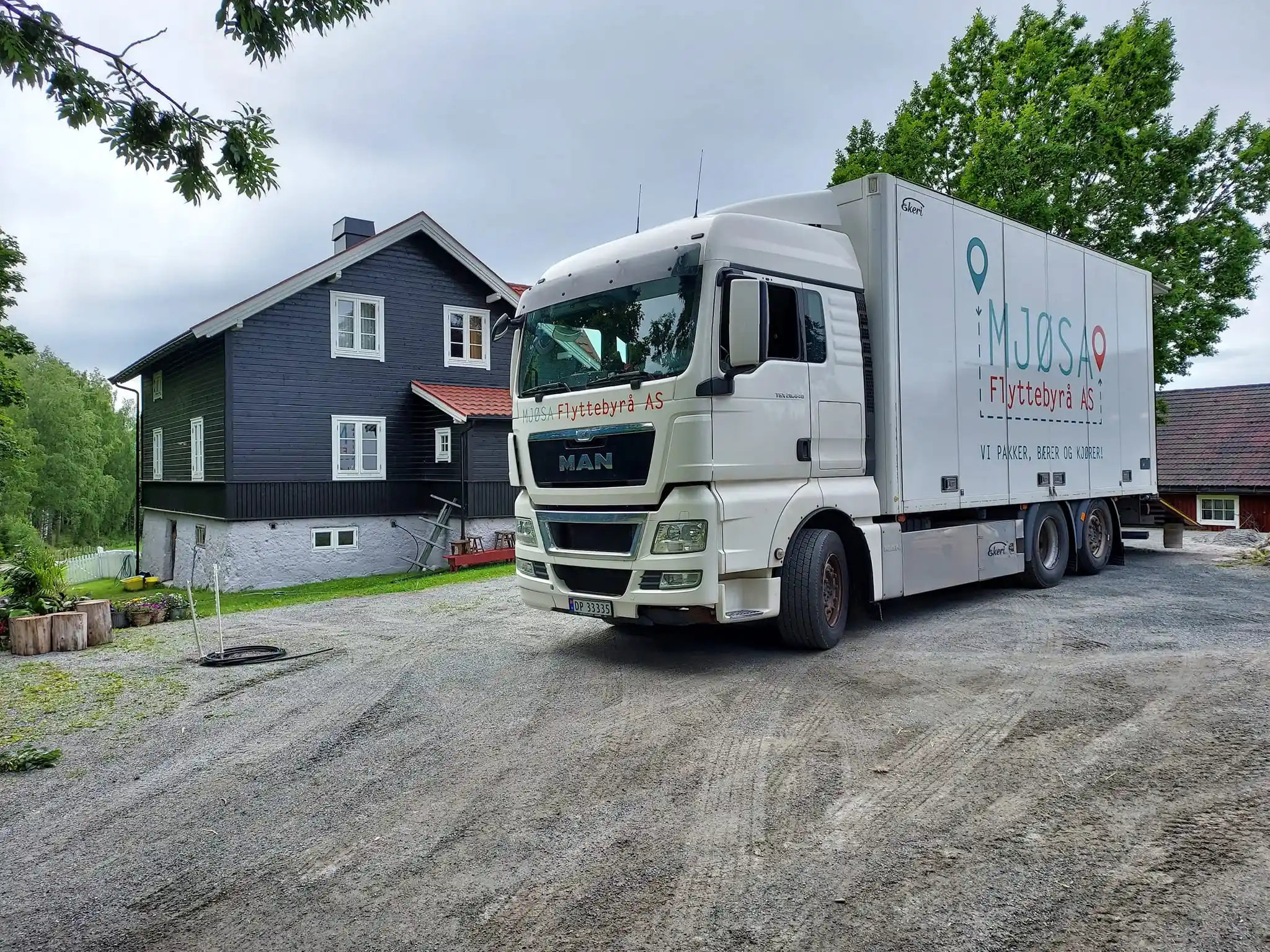 Hvit lastebil foran svart hus med rød tak.